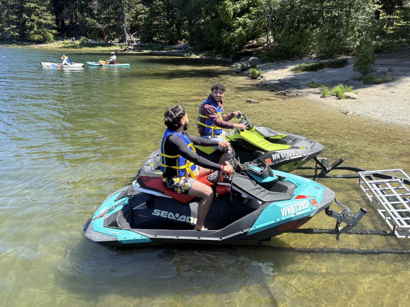 Two riders in life jackets launching Sea-Doo jet skis on a forest lake